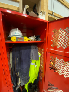 Rødt verneskap på arbeidsplass med hjelm, arbeidstøy og en gul Simple Strap stropp på øverste hylle.